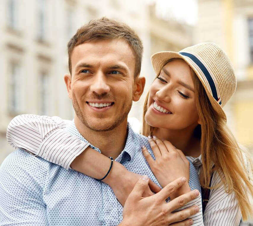 Happy couple embracing outdoors in casual summer clothing, smiling at camera.
