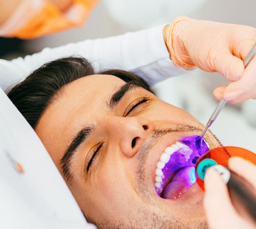 Man receiving dental treatment with colorful oral care device at dental clinic.