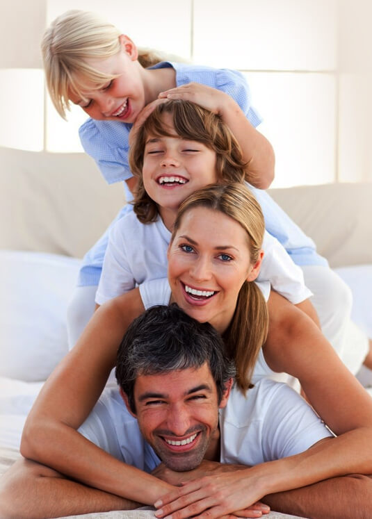 Happy family of four stacked together smiling in bright, casual home setting.