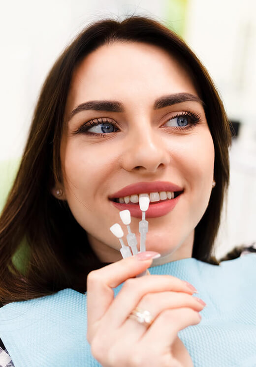Woman smiling while holding a toothbrush near her mouth in dental care setting.