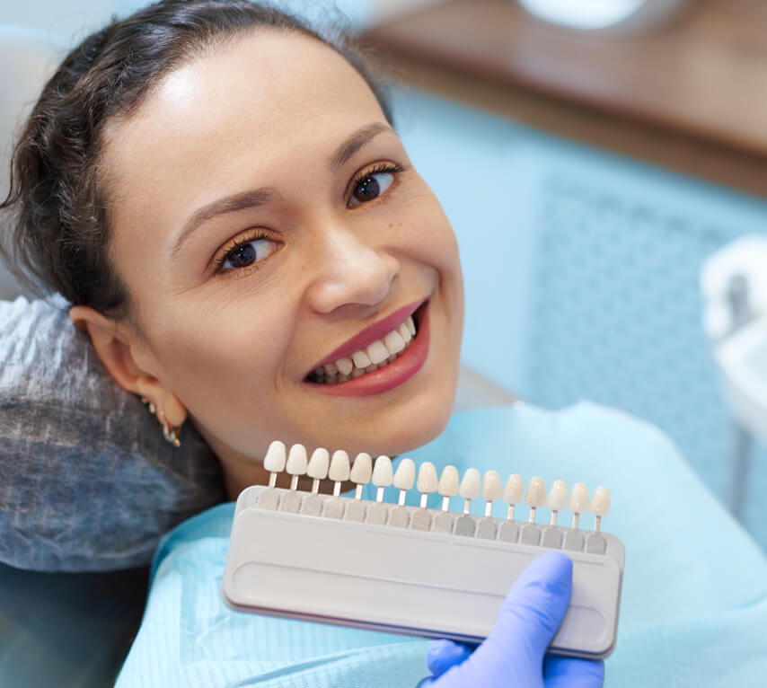 Woman holding dental shade guide at dental office, smiling at camera.