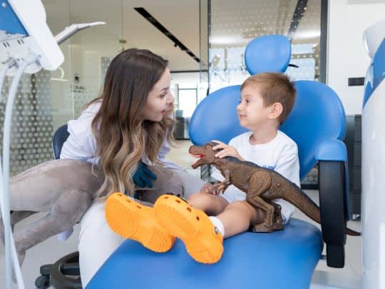 Pediatric dentist showing young boy a dental model and toy guitar in treatment chair.