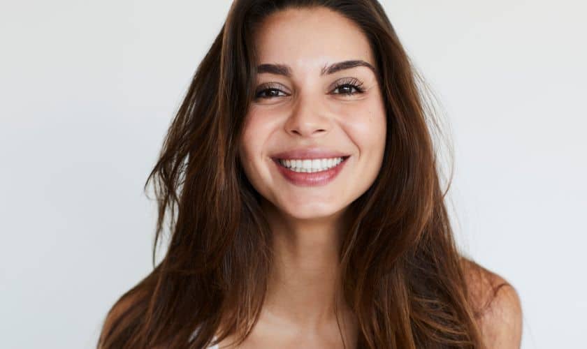 Smiling woman with long dark hair in professional headshot against white background for dental practice.