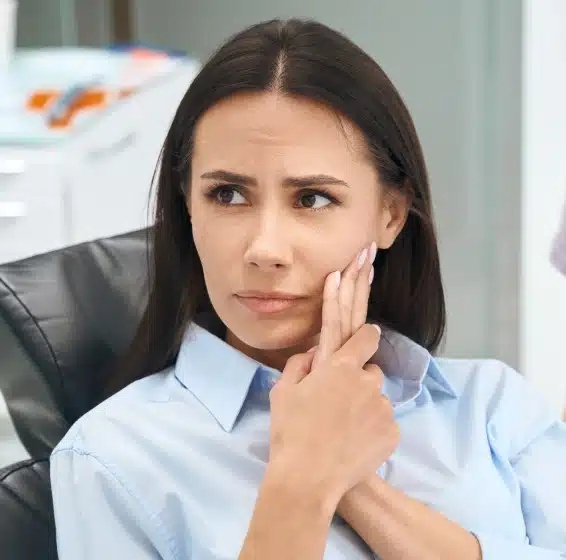 Woman in blue shirt in dental office, hand to face, thoughtful expression.