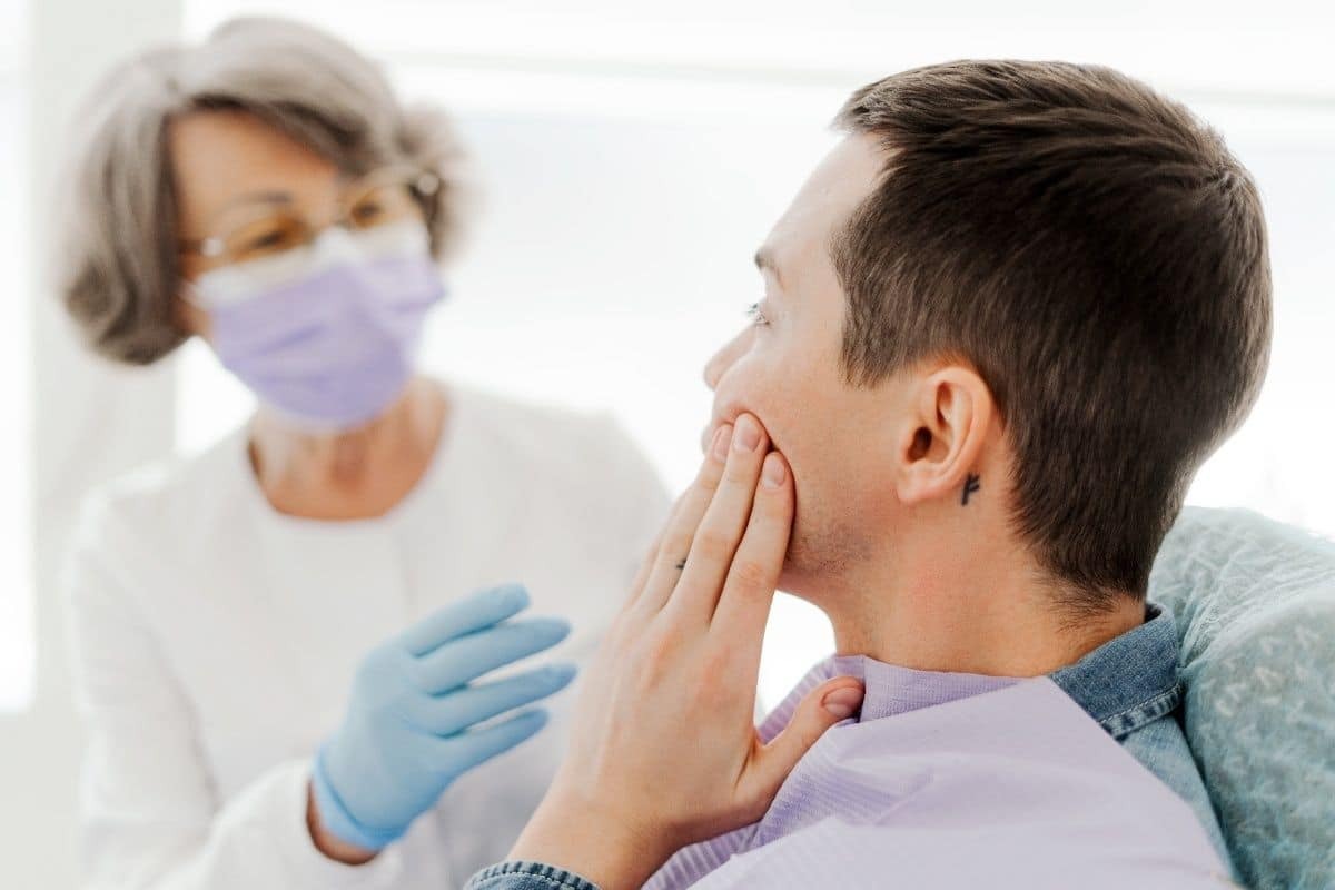 Patient experiencing tooth pain during dental consultation with masked dentist in Lee's Summit.