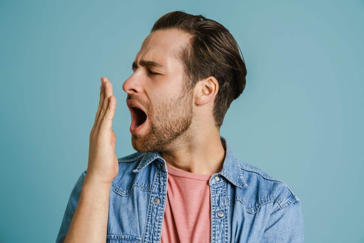 Man checking his breath by holding his hand near his mouth against a blue background.